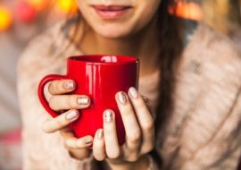 A girl holding a red color cup of tea in hand